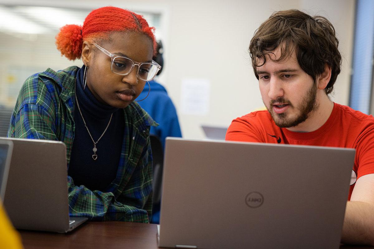 Two students looking at a laptop communicating with eachother